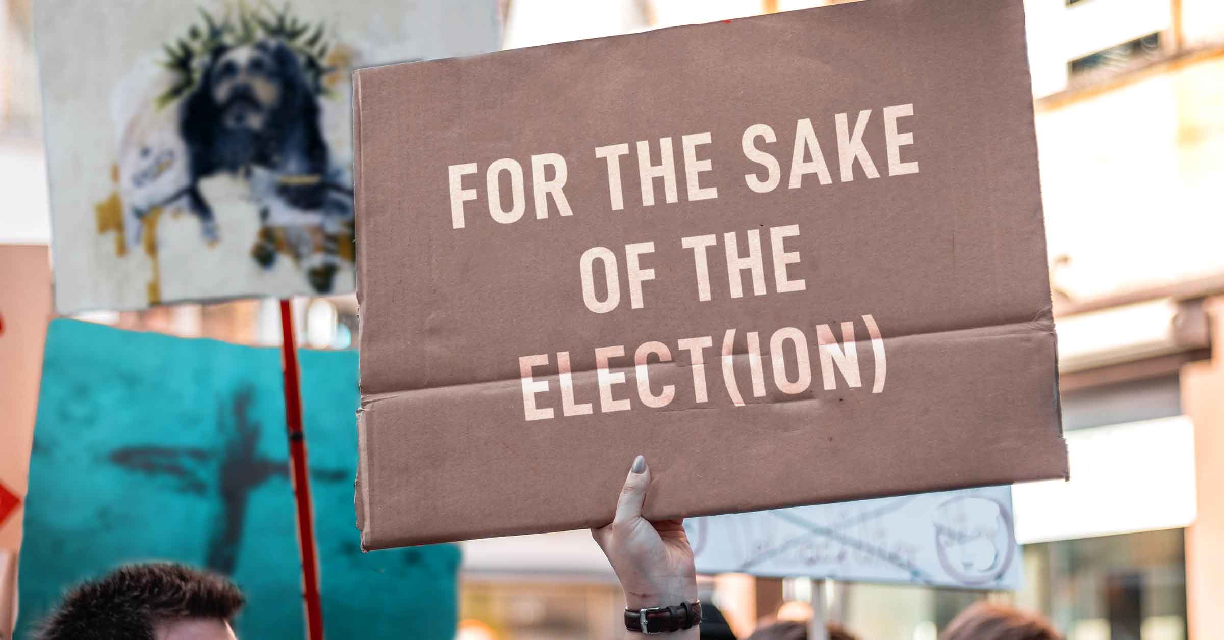 photo of person holding a sign that says "for the sake of the elect/election"